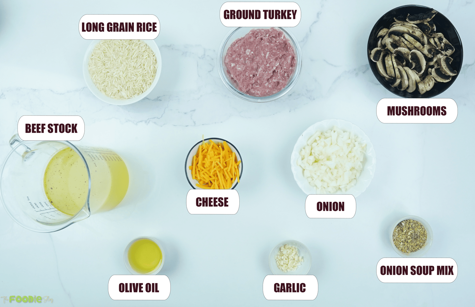 Ingredients for ground turkey casserole arranged on a counter, including ground turkey, rice, mushrooms, onion, garlic, beef stock, shredded cheese, onion soup mix, and olive oil