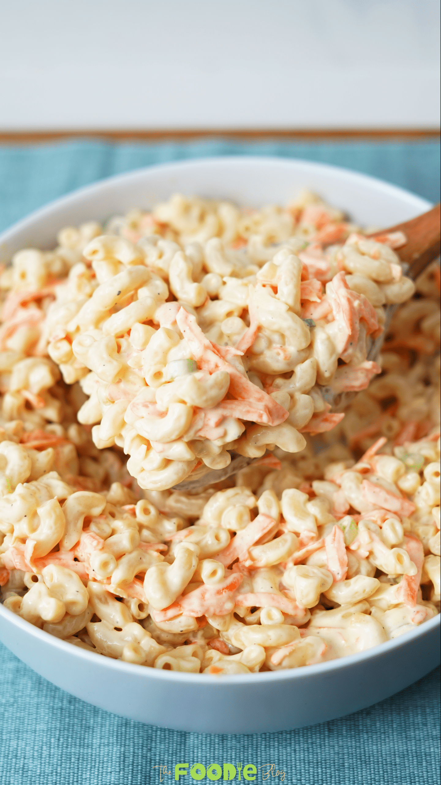 Close-up spoonful of Hawaiian macaroni salad showing creamy macaroni, shredded carrot, and green onion