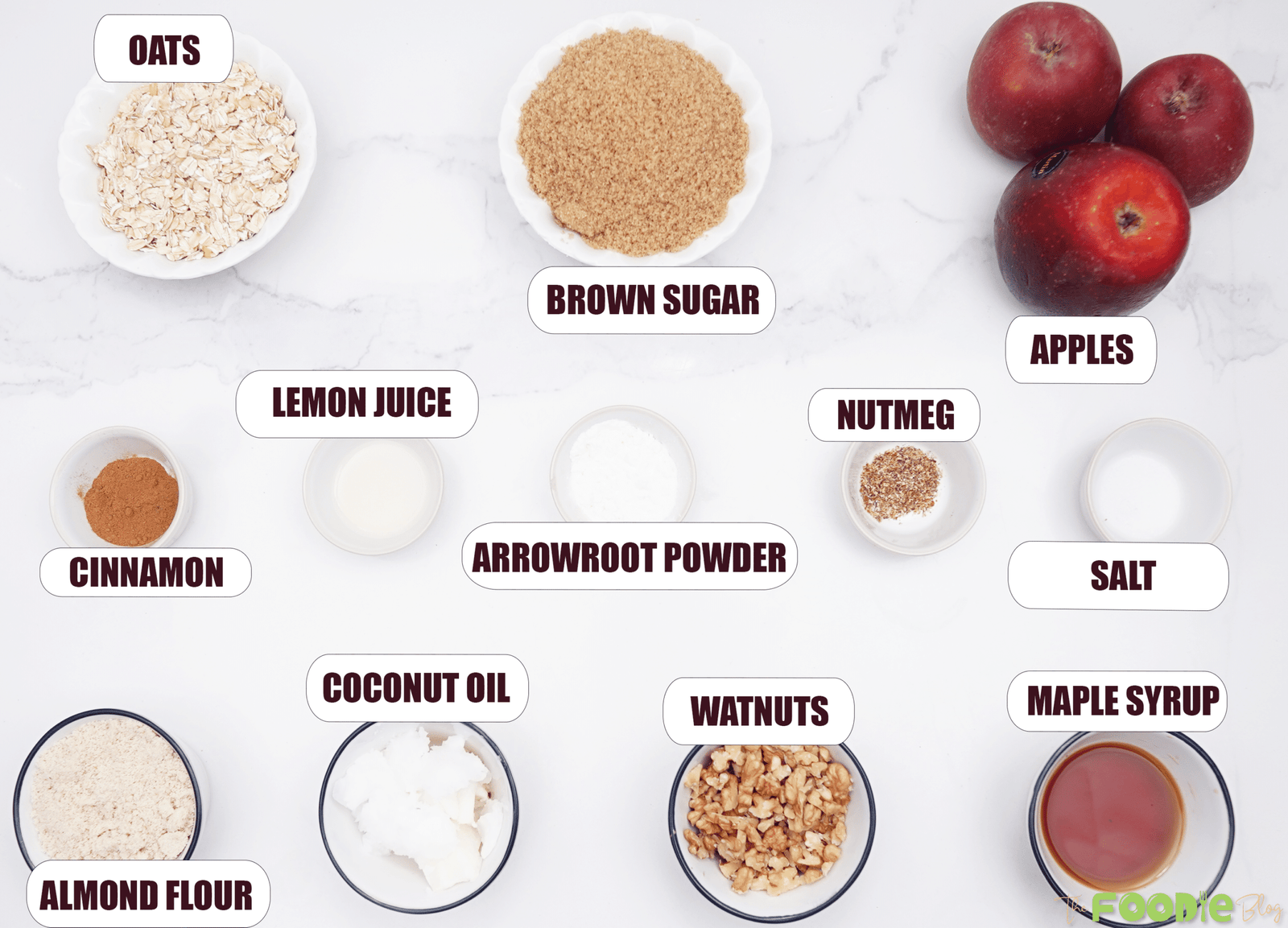 Overhead view of apples, oats, brown sugar, maple syrup, almond flour, coconut oil, walnuts, cinnamon, nutmeg, salt, lemon juice, and arrowroot powder for healthy apple crisp