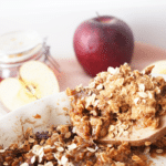 Wooden spoon lifting a serving of healthy apple crisp with oats and tender apples from a baking dish