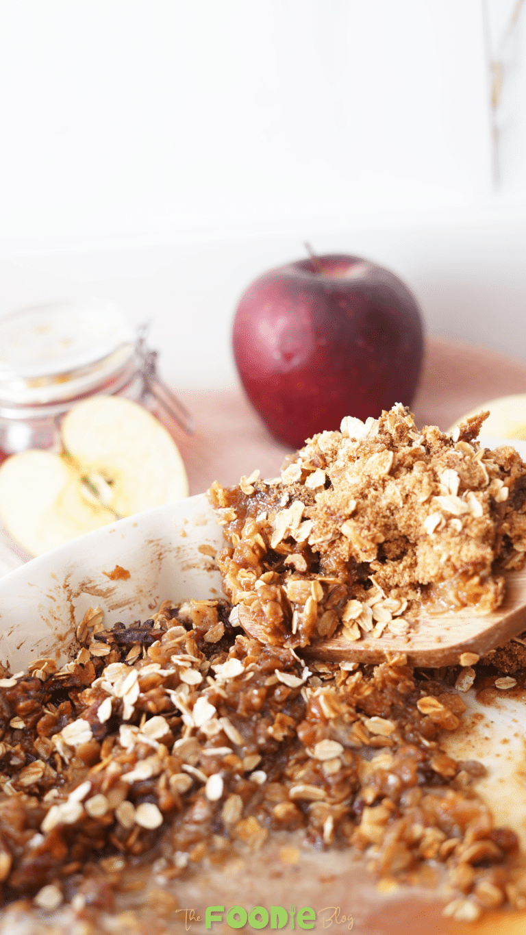 Wooden spoon lifting a serving of healthy apple crisp with oats and tender apples from a baking dish