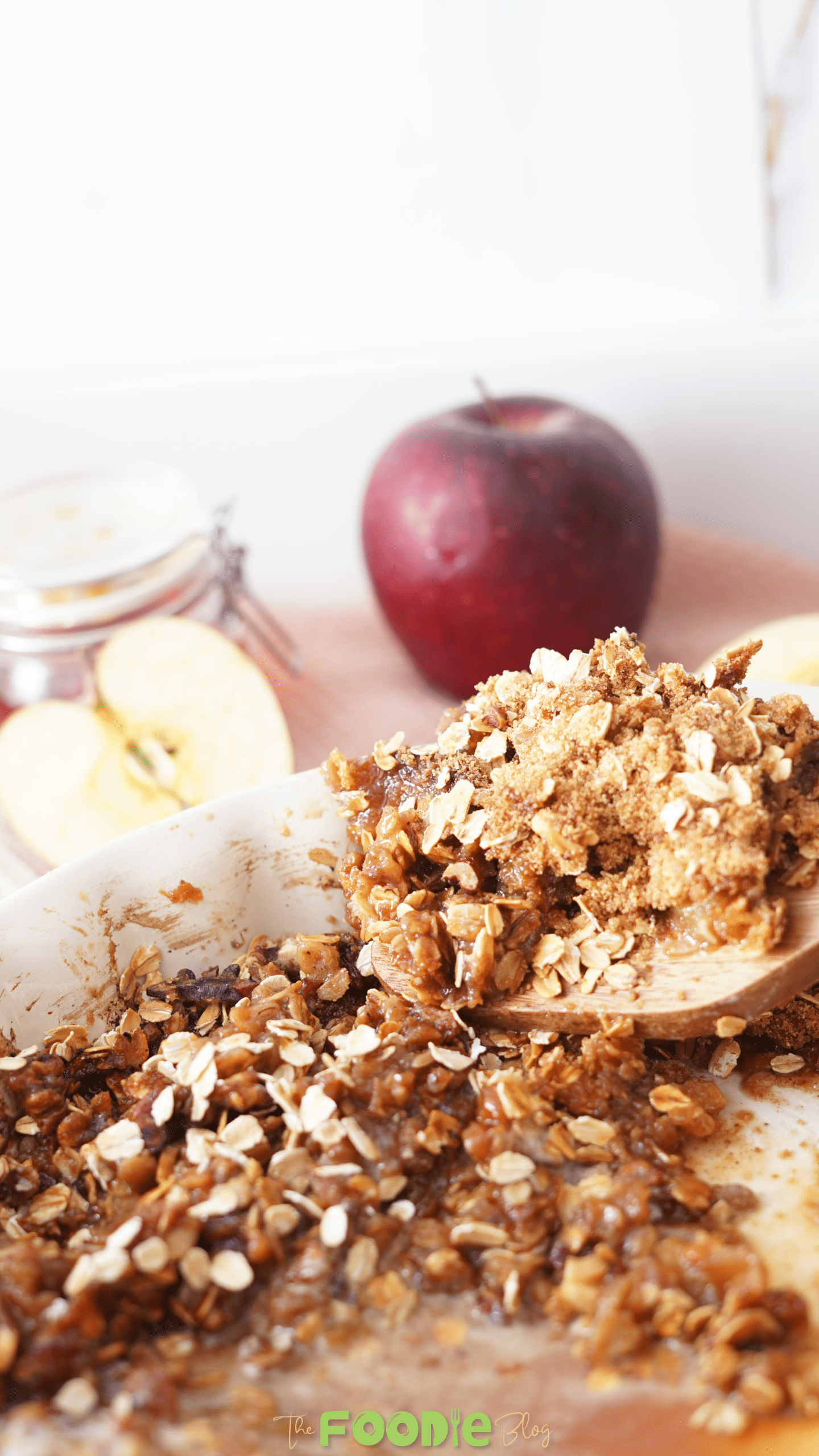 Wooden spoon lifting a serving of healthy apple crisp with oats and tender apples from a baking dish