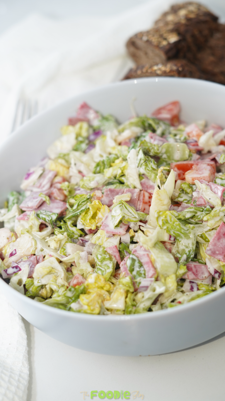 A white bowl filled with creamy hoagie dip made with chopped lettuce, salami, pepperoni, provolone, tomatoes, and red onion.