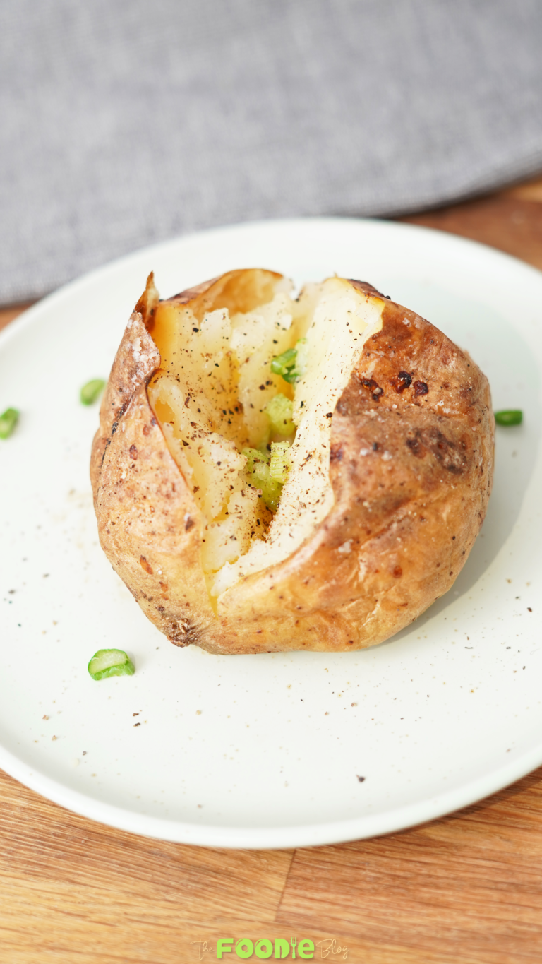 Close-up of a baked potato with crisp golden skin, fluffy center, black pepper, salt, and green onion.