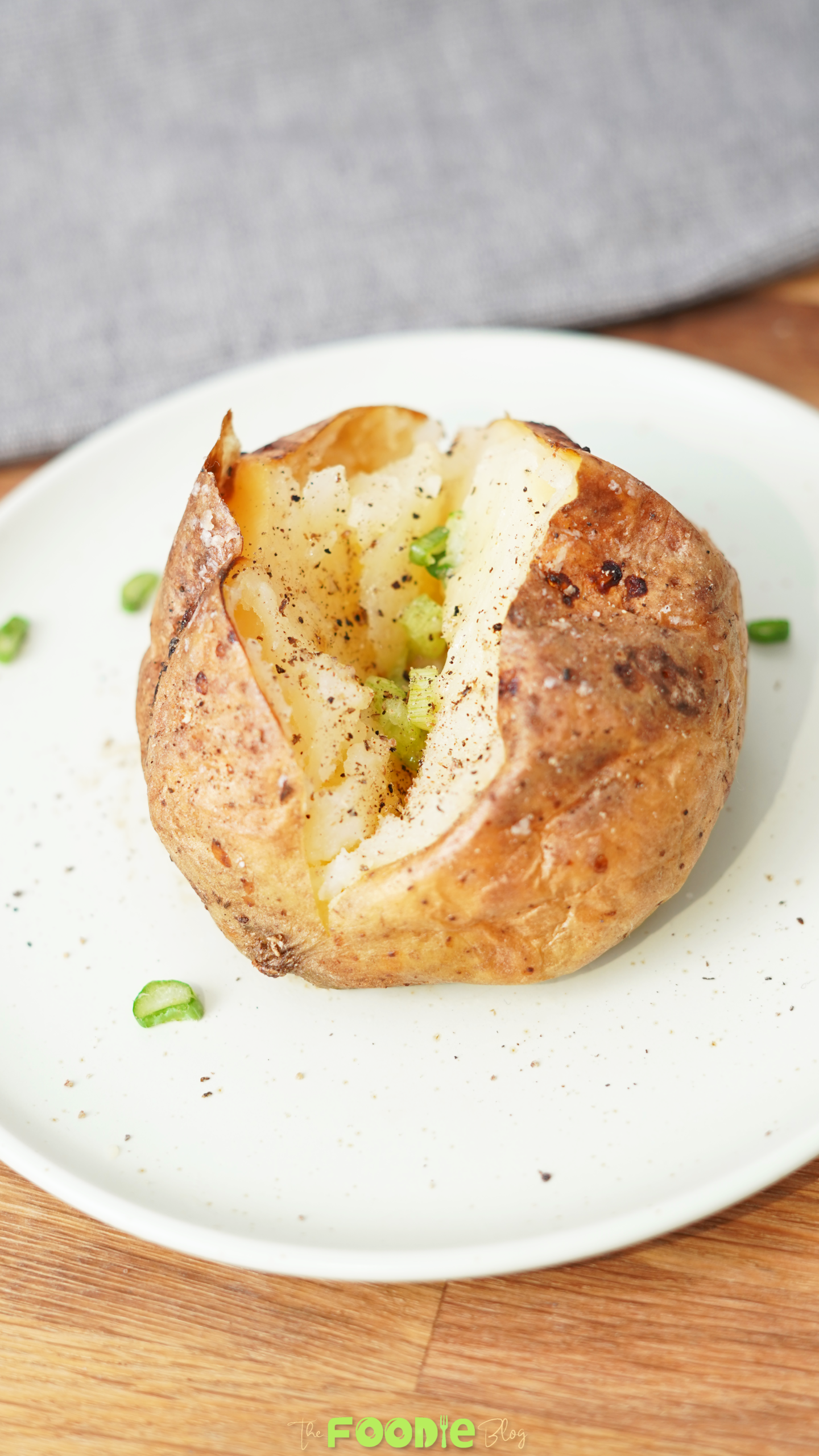 Close-up of a baked potato with crisp golden skin, fluffy center, black pepper, salt, and green onion.