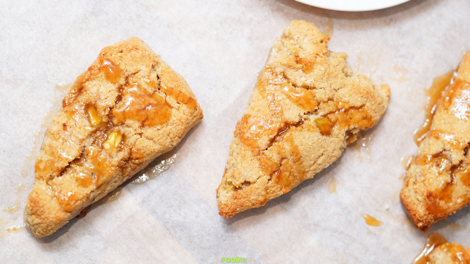 Baked keto caramel apple scones on parchment paper with caramel sauce drizzled over the tops.