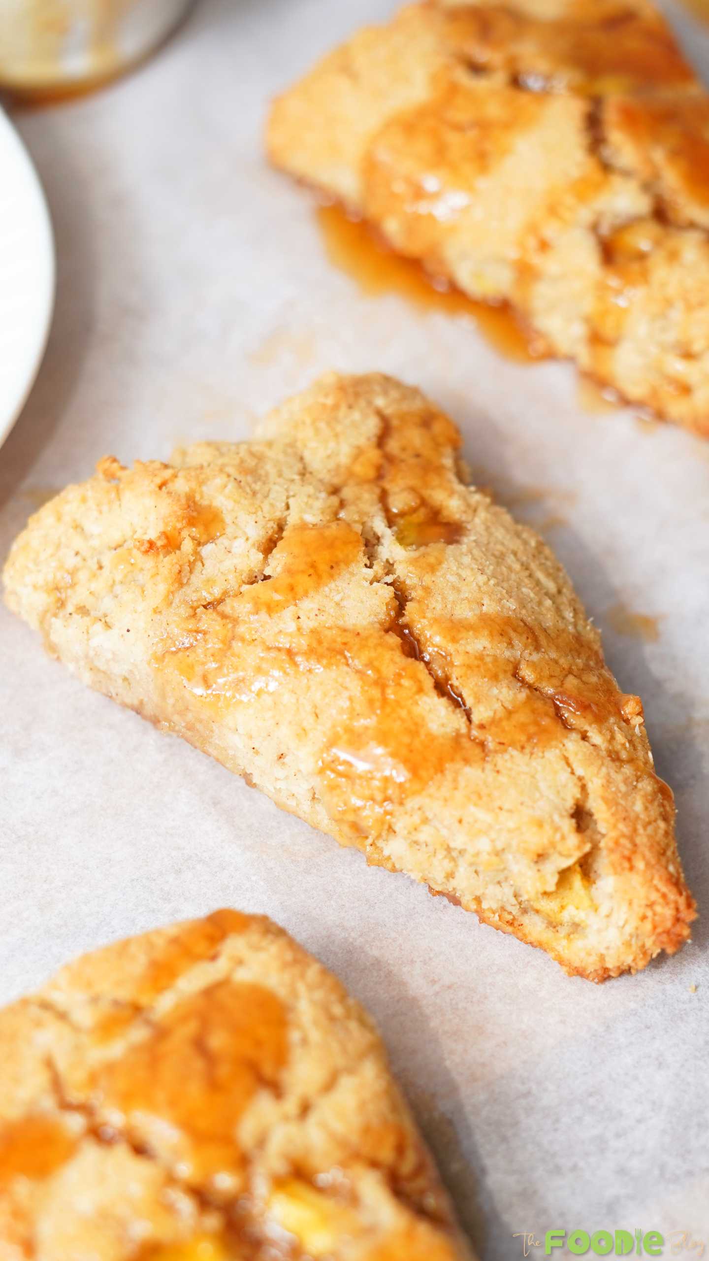 Close-up of a golden keto apple scone on parchment paper with sugar-free caramel sauce drizzled over the top.