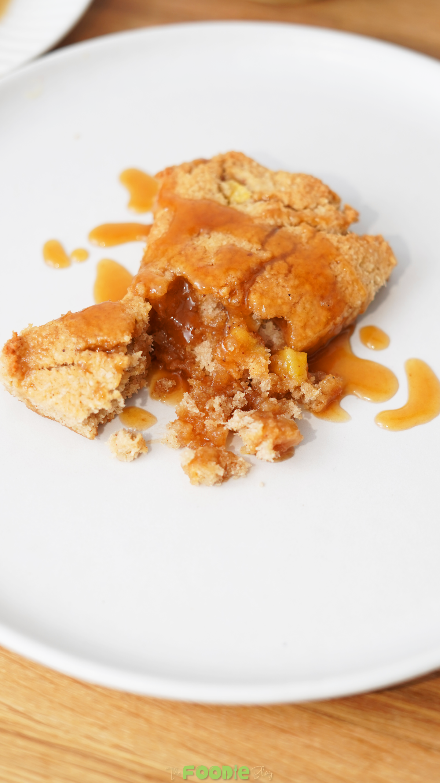 A broken keto caramel apple scone on a white plate with caramel sauce drizzled over the crumb and plate.