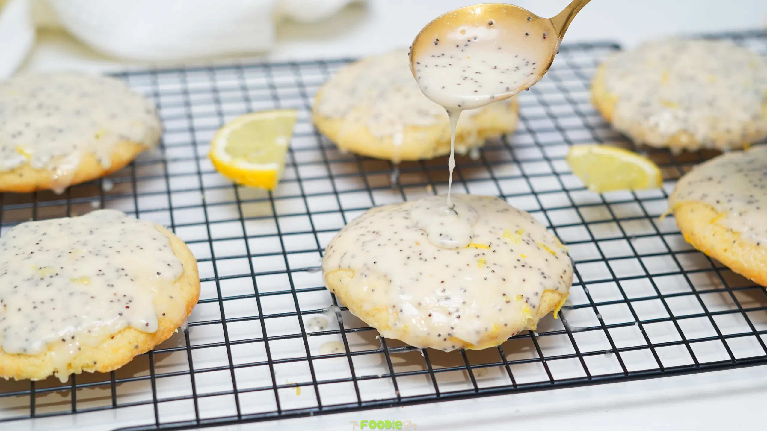 Soft glazed lemon poppy seed cookies cooling on a wire rack with fresh lemon slices