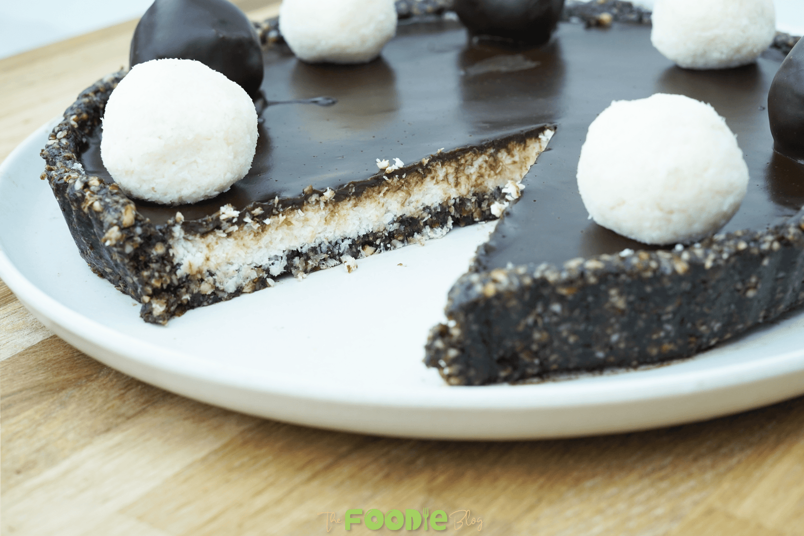 Single slice of No-Bake Vegan Bounty Tart topped with a coconut truffle on a wooden surface