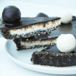 Whole No-Bake Vegan Bounty Tart with one slice removed and coconut truffles on top