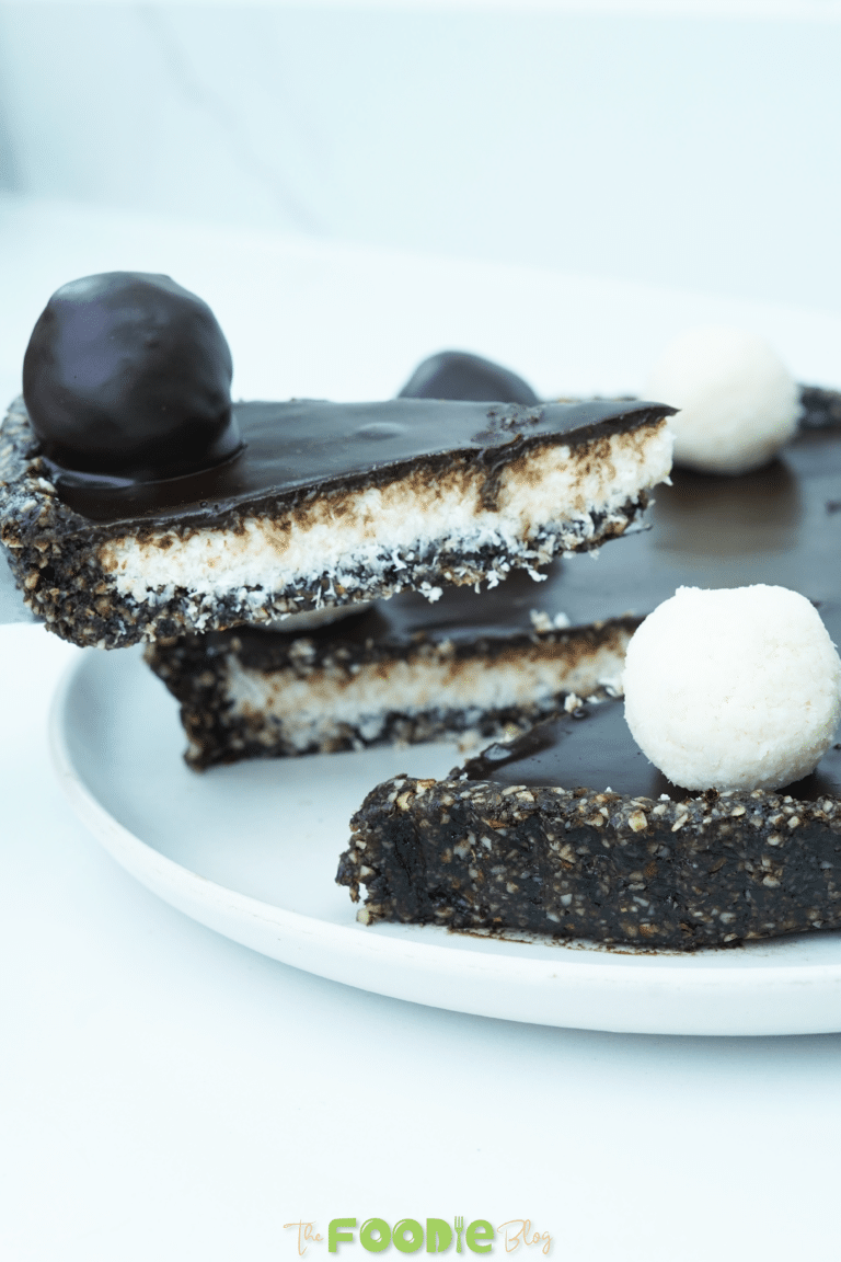 Whole No-Bake Vegan Bounty Tart with one slice removed and coconut truffles on top