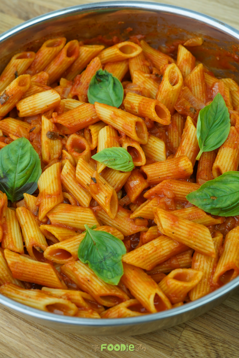 Tomato-coated penne in a pan with basil leaves on top