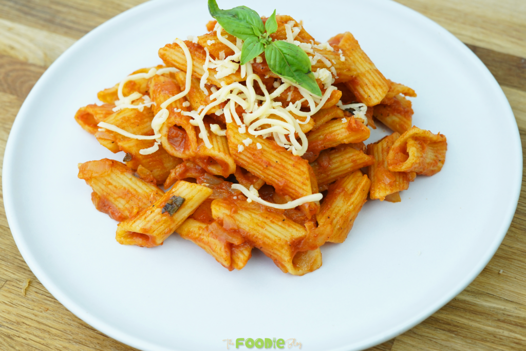 Plated penne tossed in tomato sauce topped with Parmesan and fresh basil