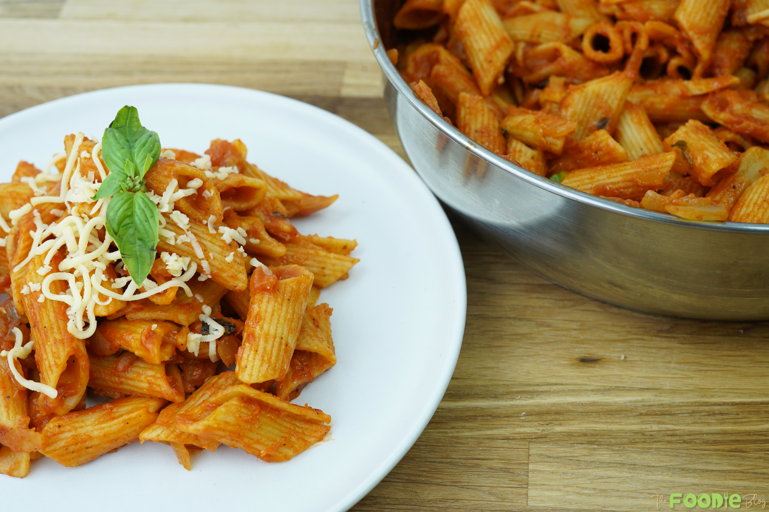 Plated tomato pasta with basil and Parmesan next to the pot of pasta