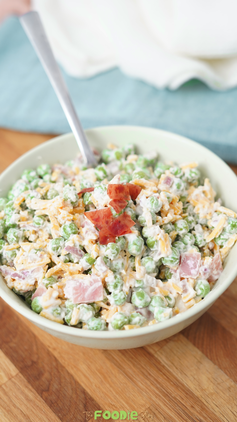 Close-up of creamy pea salad in a bowl topped with chopped bacon and mixed with cheddar cheese and red onion.