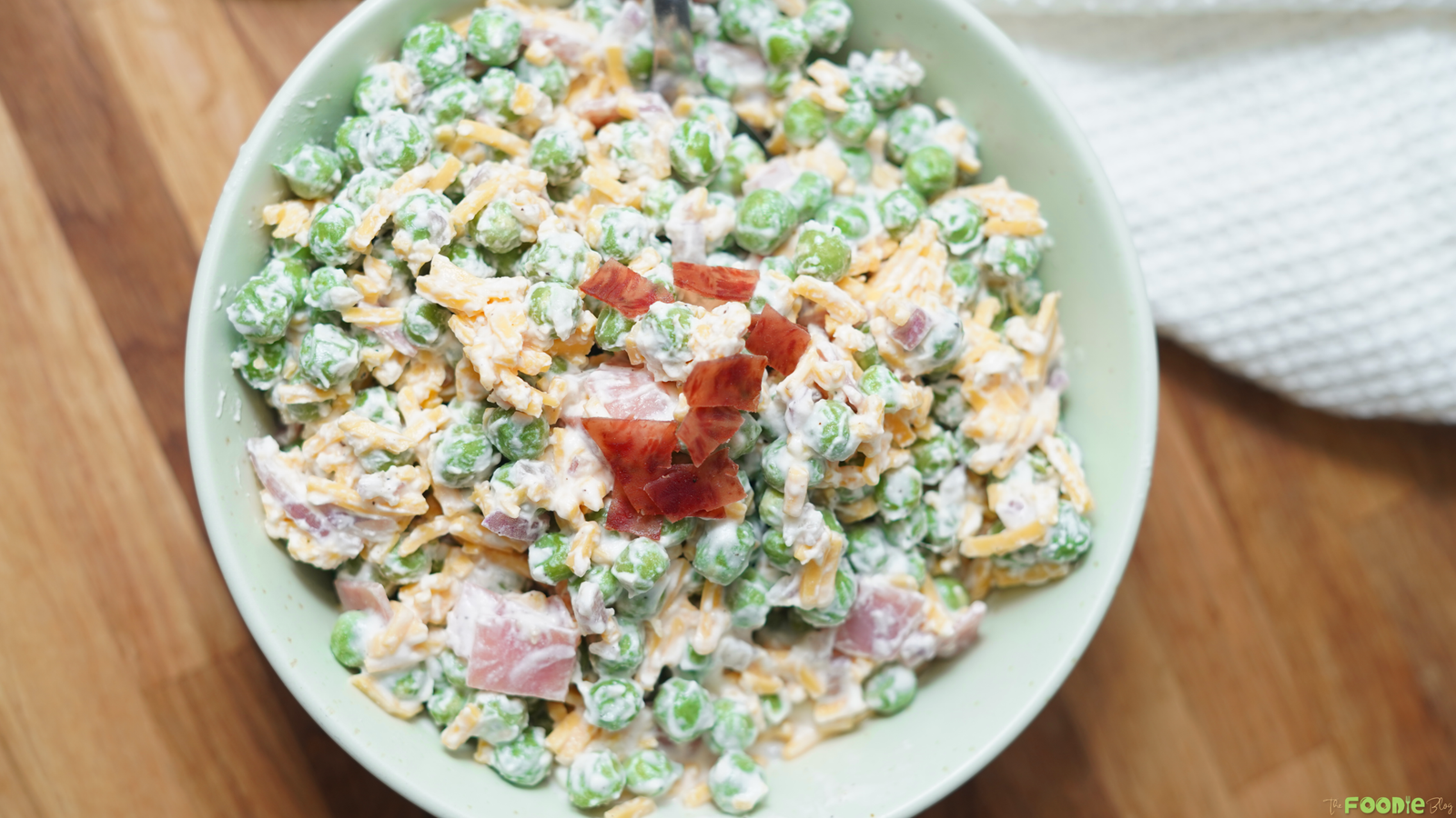 Overhead view of pea salad in a bowl with green peas, cheddar cheese, bacon, red onion, and creamy dressing