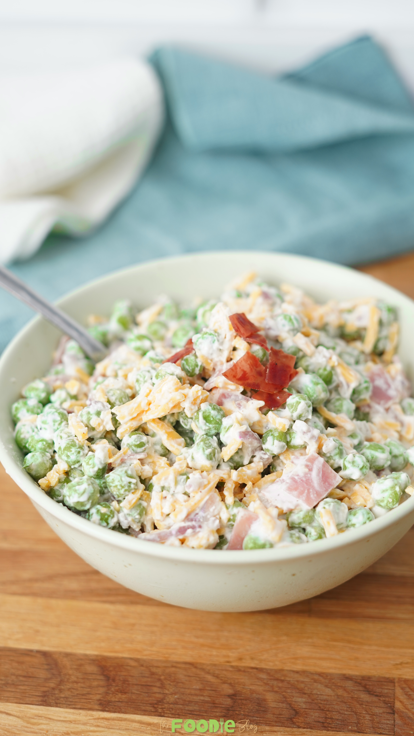 Creamy pea salad served in a bowl with green peas, shredded cheddar cheese, bacon pieces, and a creamy dressing.