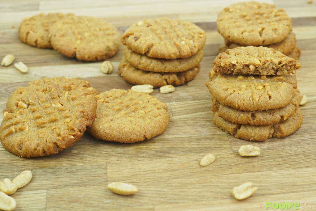 several peanut butter cookies arranged on a wooden board with scattered peanuts