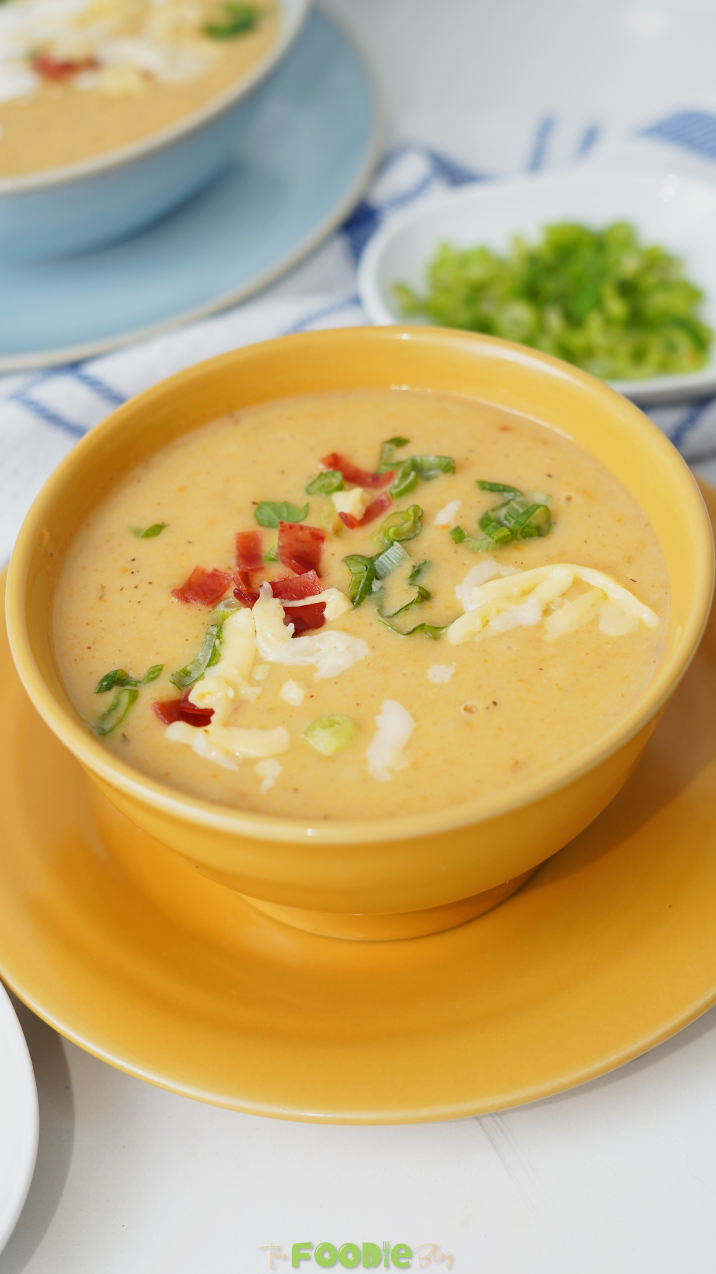 Close-up of creamy potato soup in a yellow bowl with green onions, bacon bits, and cheese on top