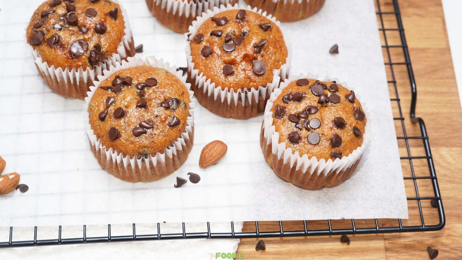Golden protein muffins with chocolate chips cooling on a wire rack lined with parchment paper.