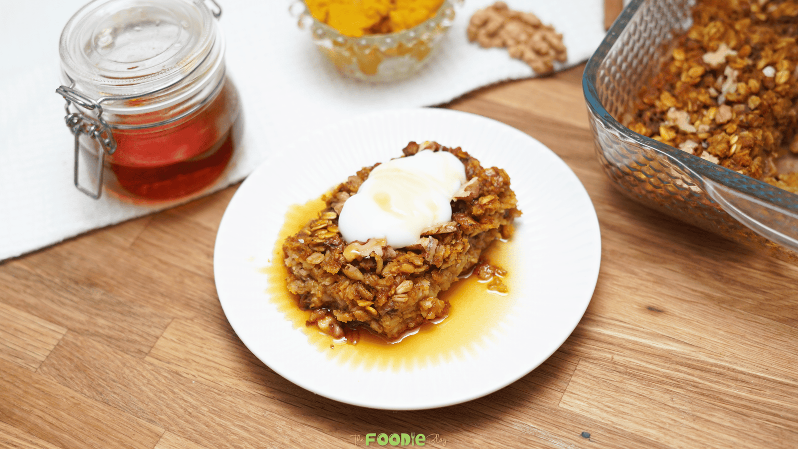 Slice of pumpkin baked oatmeal on a white plate topped with yogurt and maple syrup beside the baking dish