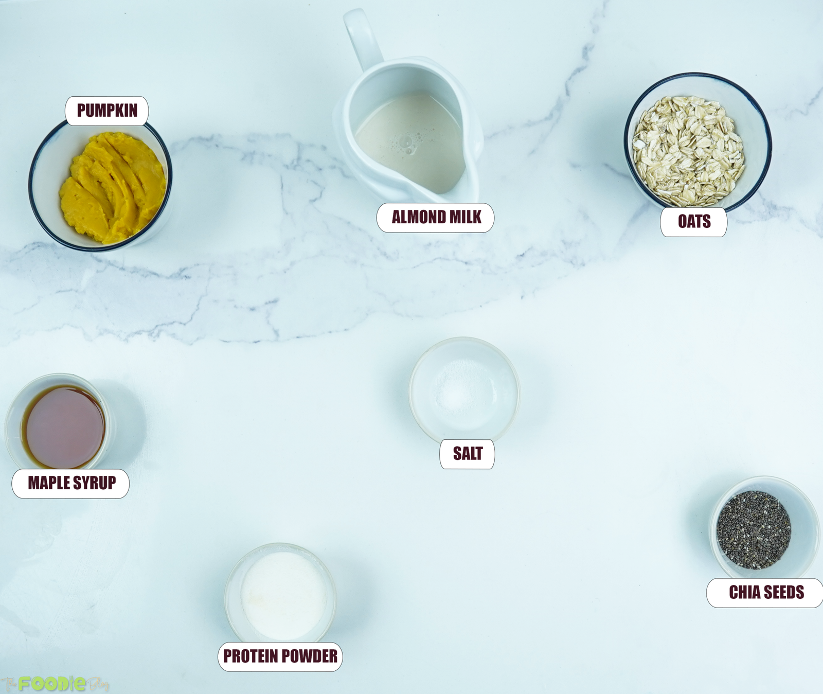 Overhead view of ingredients for pumpkin pie overnight oats including pumpkin puree, almond milk, oats, chia seeds, maple syrup, protein powder, and salt.