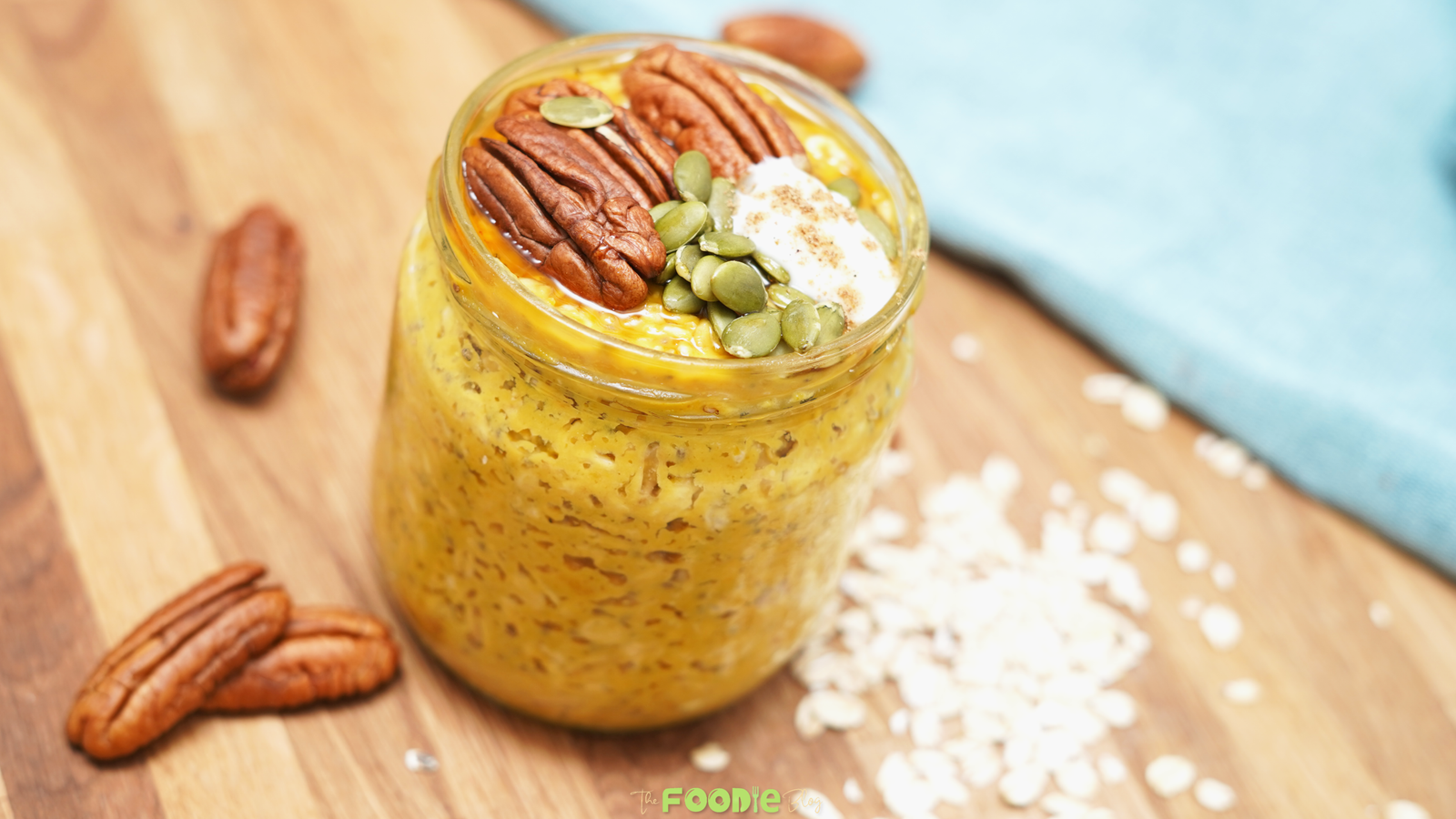 Jar of pumpkin pie overnight oats topped with pecans, pepitas, coconut whipped cream, and maple syrup on a wooden board.