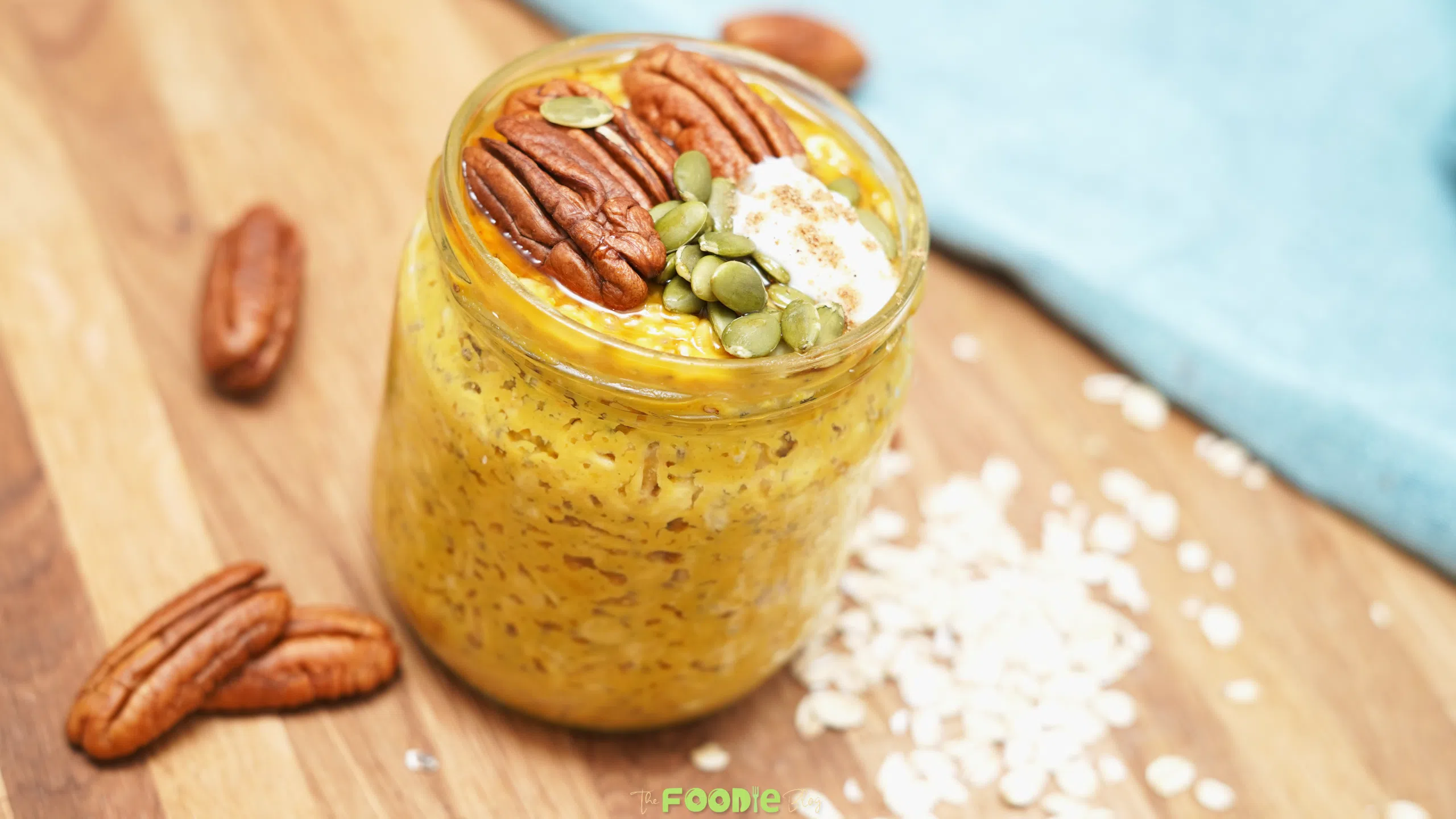 Jar of pumpkin pie overnight oats topped with pecans, pepitas, coconut whipped cream, and maple syrup on a wooden board.