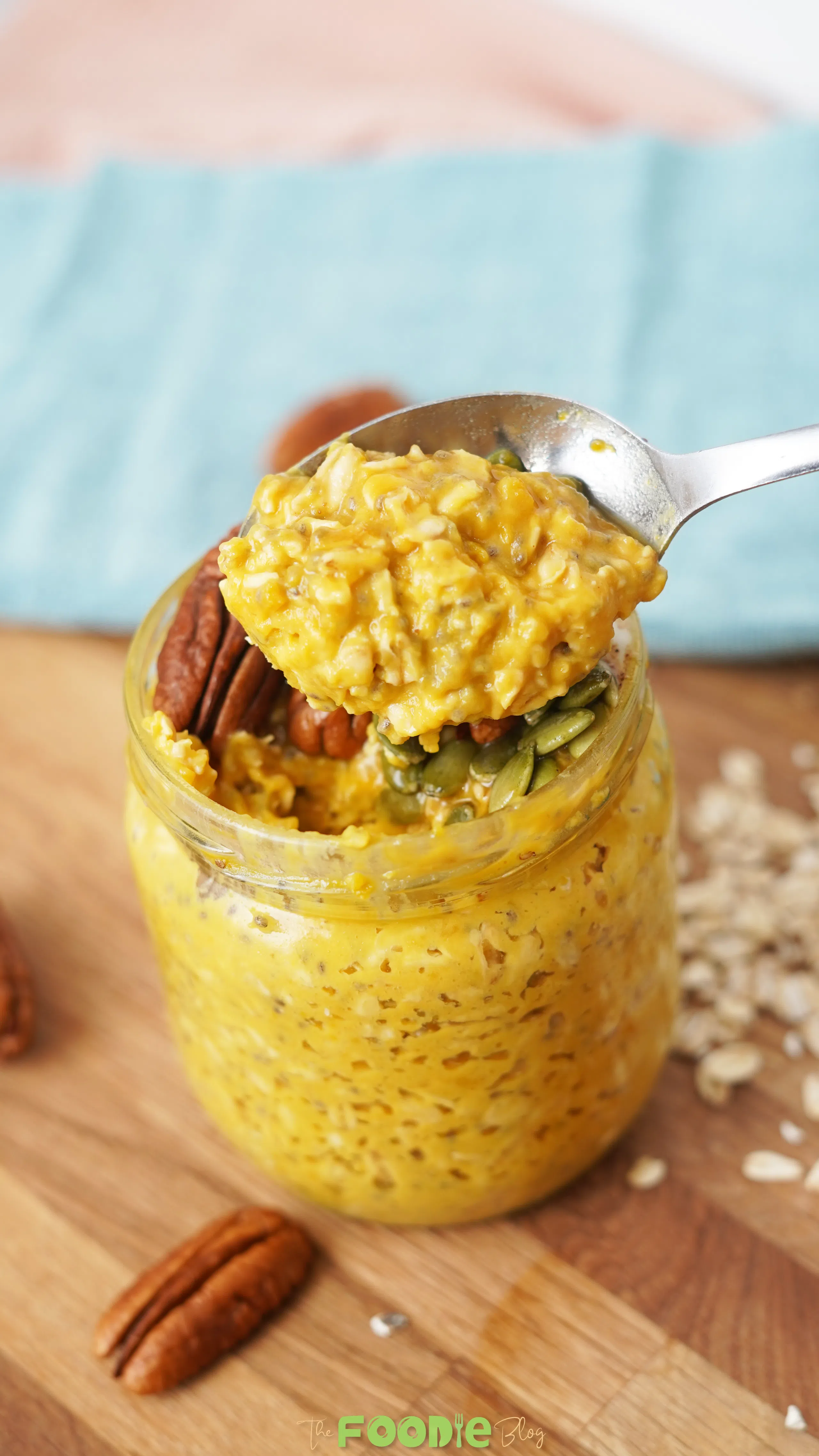 Spoonful of creamy pumpkin pie overnight oats lifted from a jar with pecans and pumpkin seeds on top.