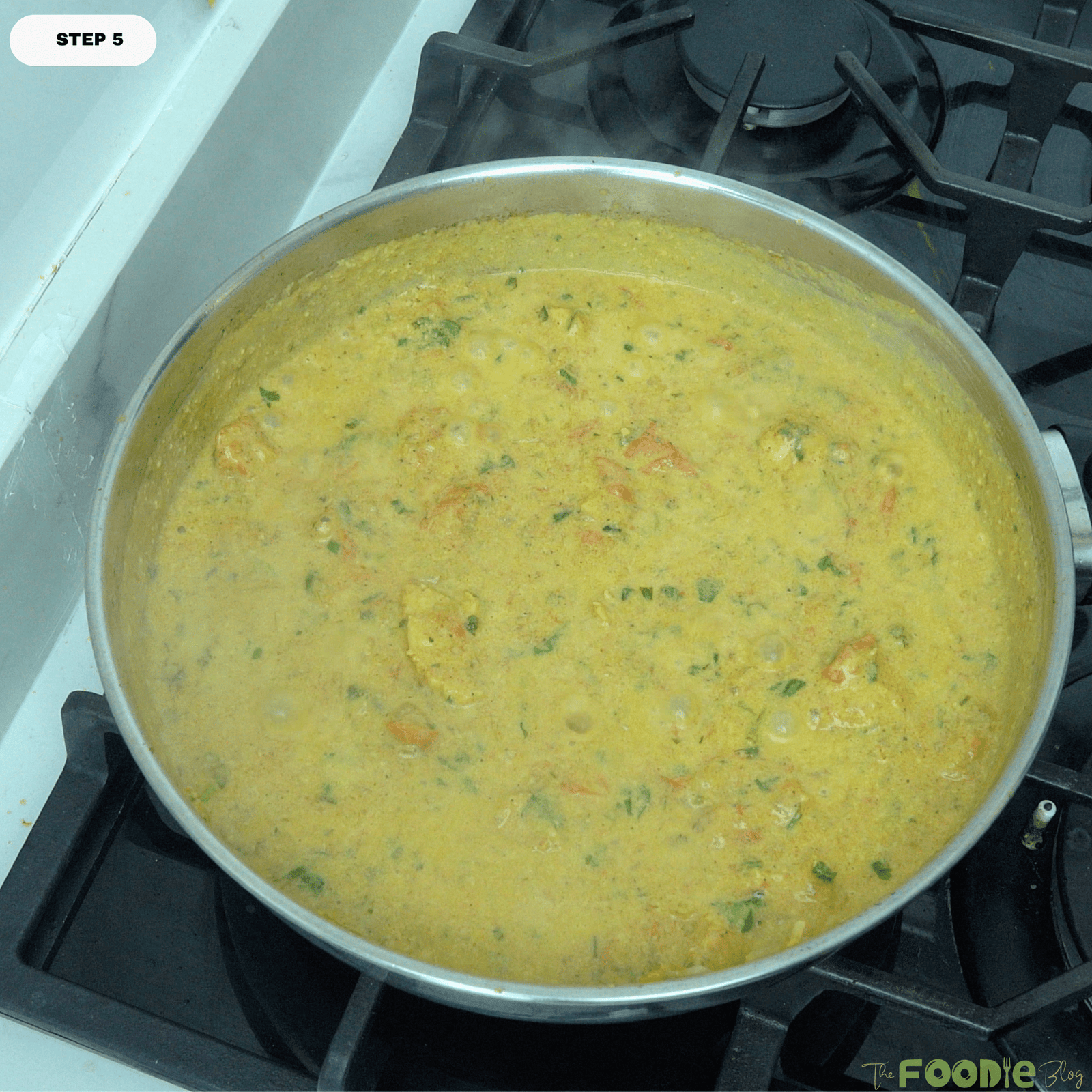 Finished chicken curry simmering in a pan with creamy golden sauce and chopped herbs