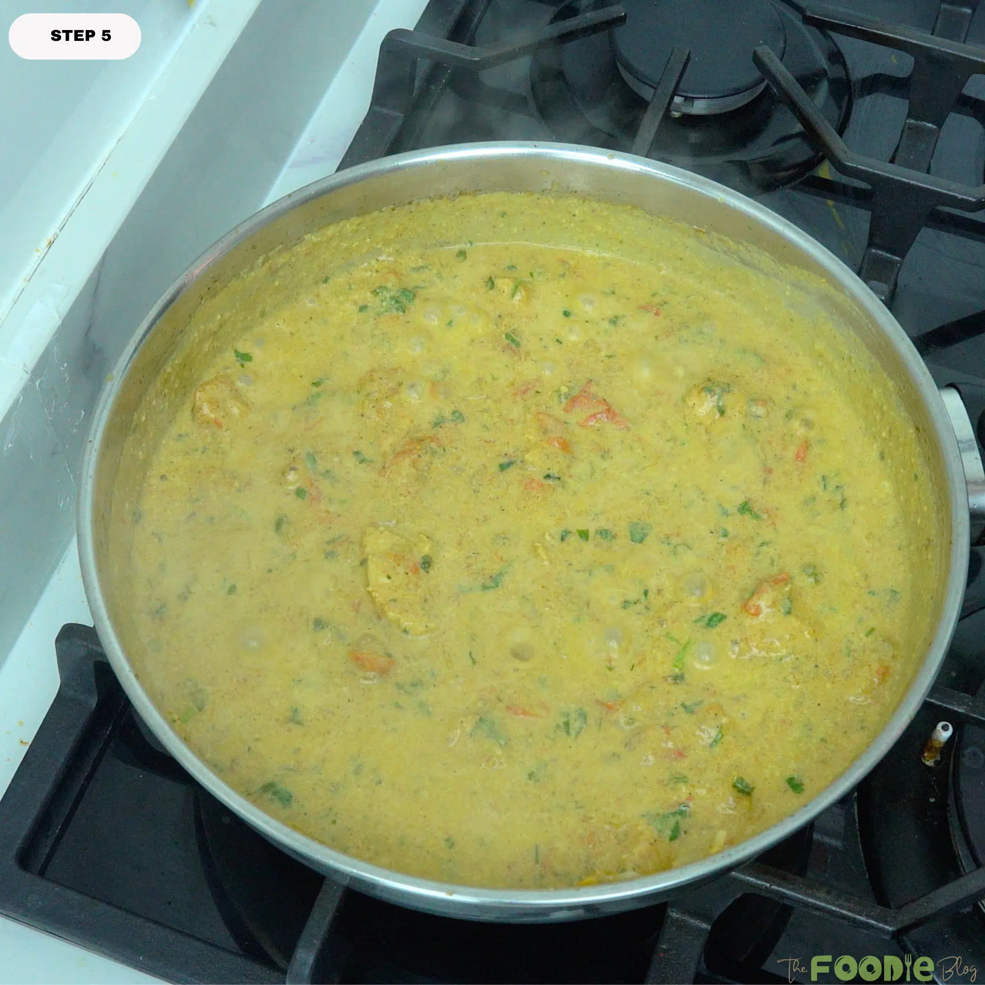 Finished chicken curry simmering in a pan with creamy golden sauce and chopped herbs