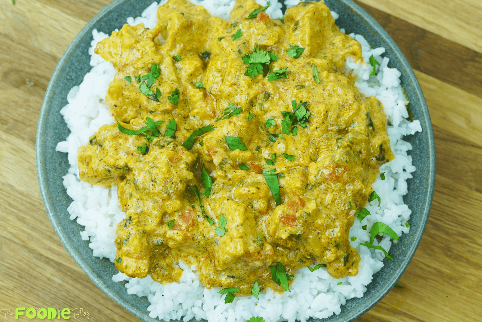 Overhead bowl of creamy chicken curry on white rice with chopped cilantro garnish