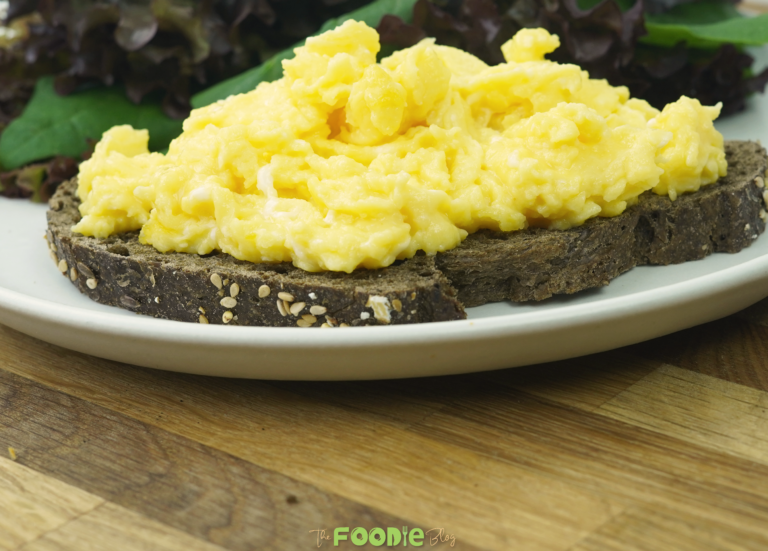 scrambled eggs served on dark toasted bread with salad leaves in the background