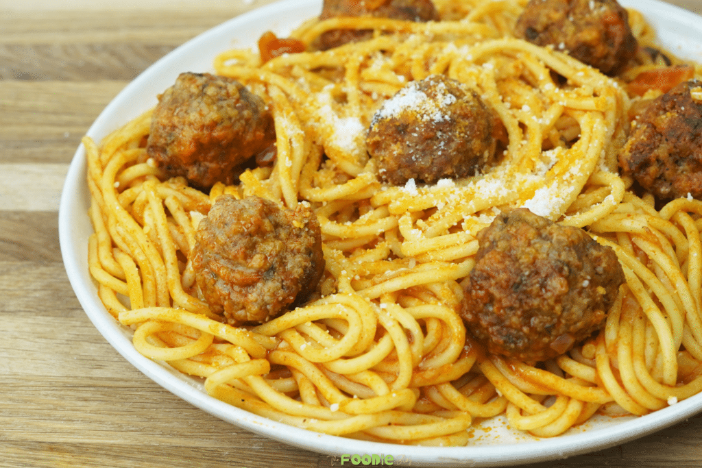 serving view of spaghetti and meatballs on a white plate with tomato sauce and Parmesan