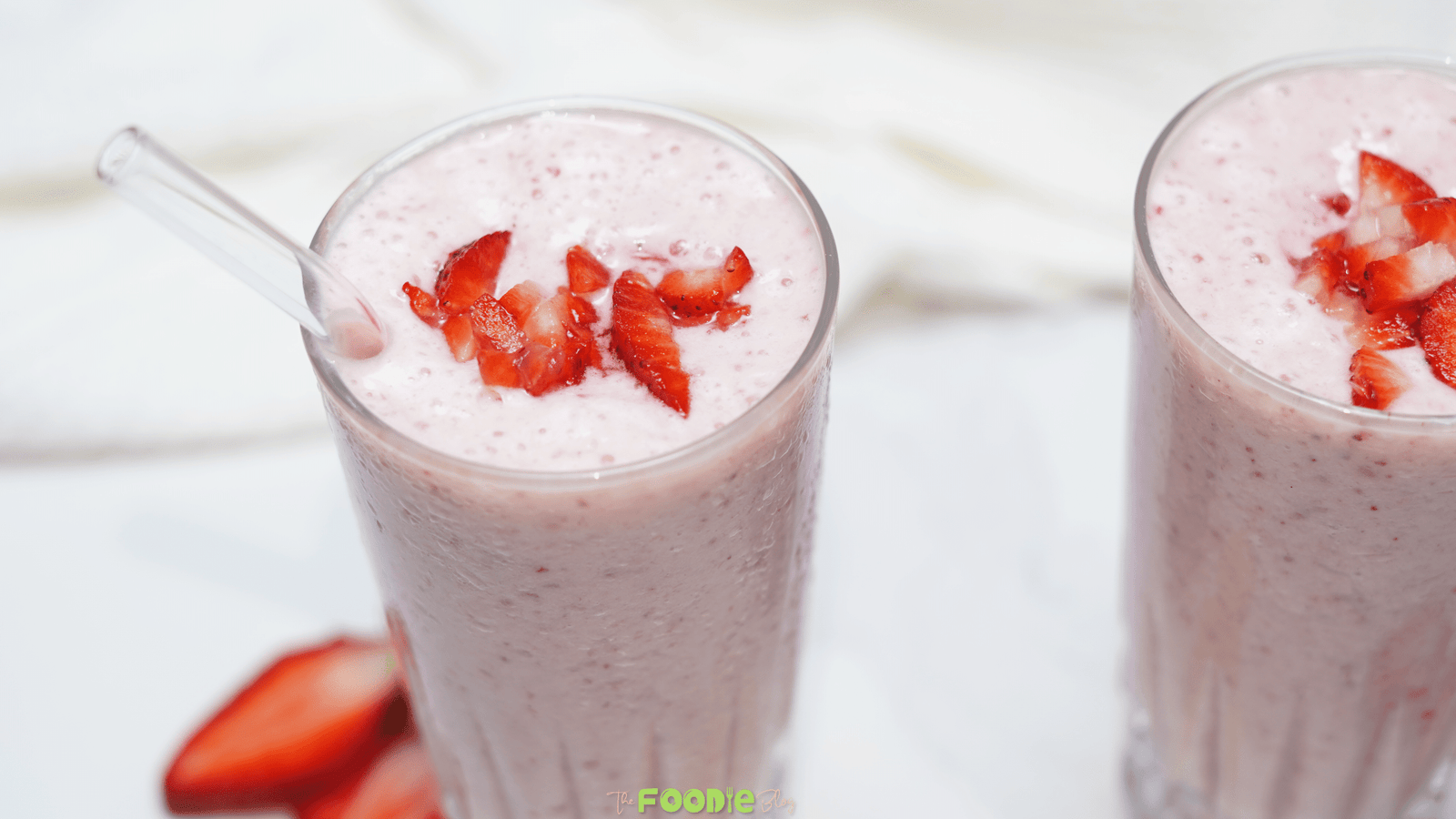 Two tall glasses of strawberry banana smoothie topped with chopped strawberries