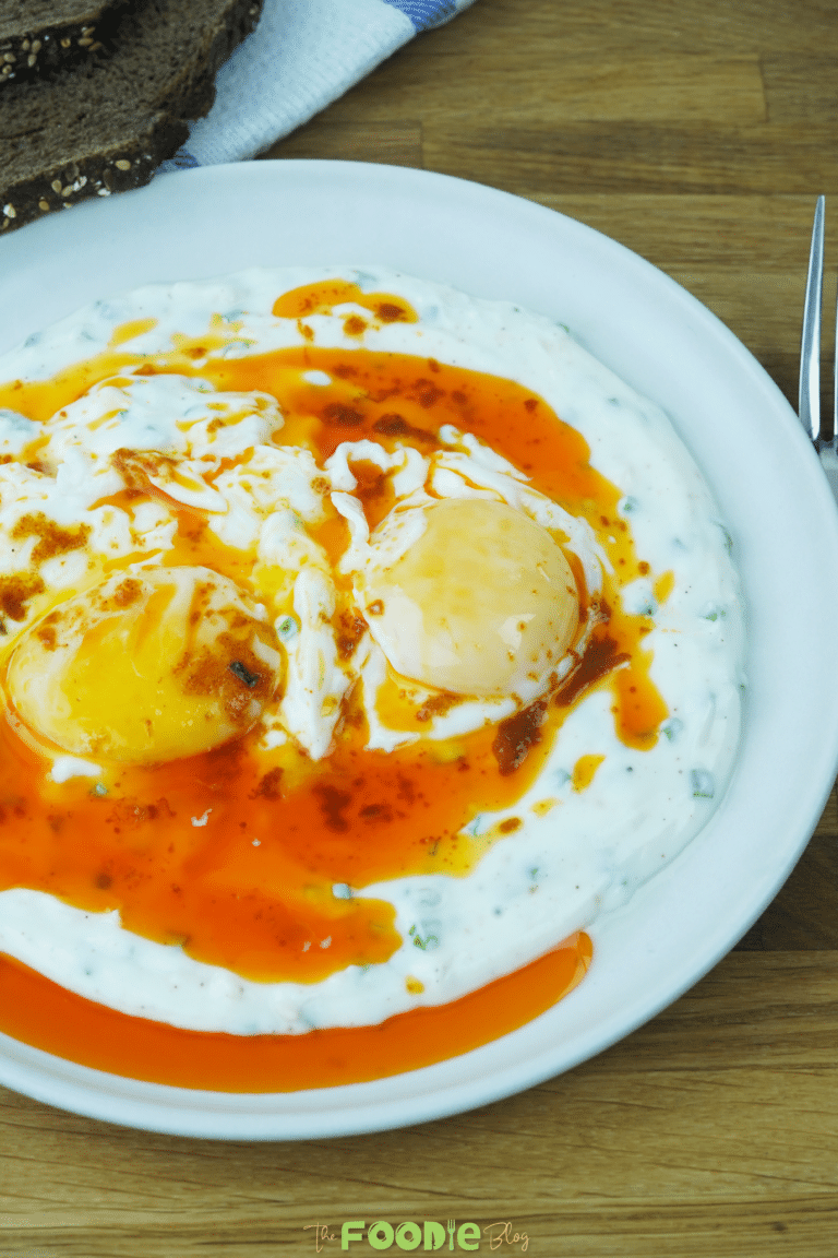 Final plated Turkish eggs with poached eggs over creamy yogurt and paprika butter on a white plate