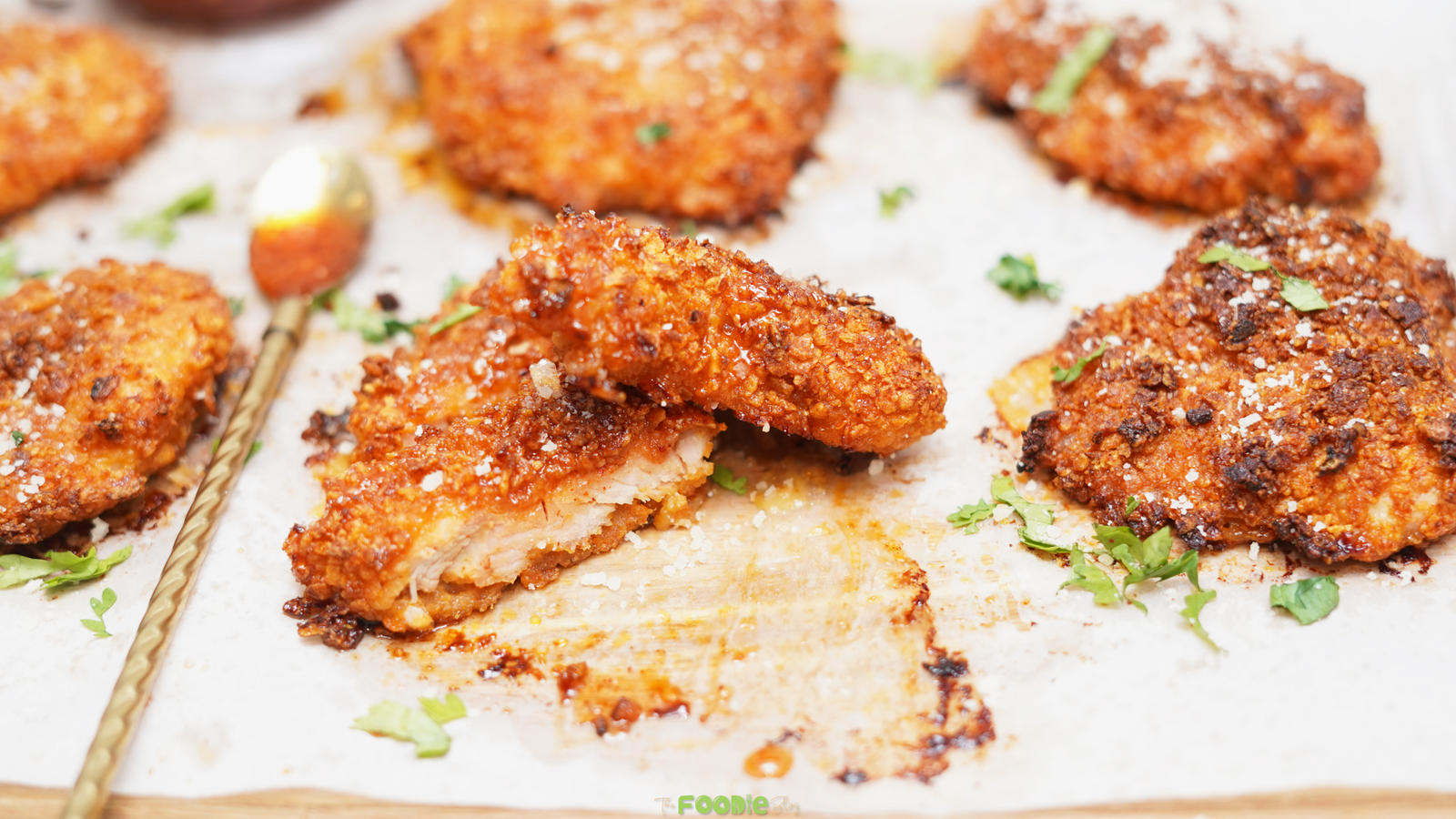 Close-up of sliced crunchy hot honey chicken with a golden cornflake crust, fresh herbs, Parmesan, and sauce drizzles.