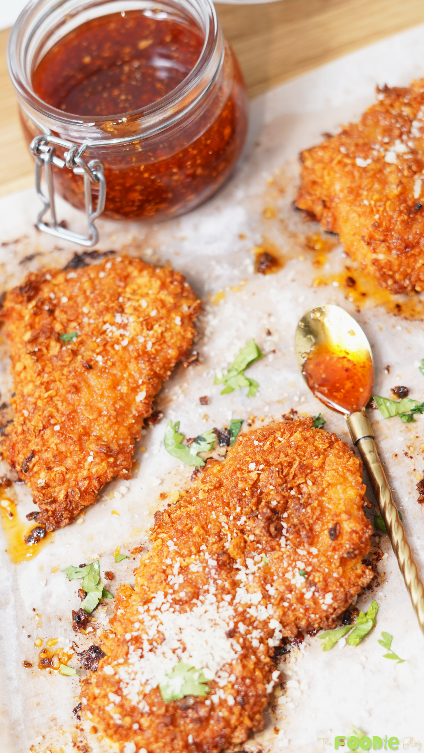 Crunchy baked chicken pieces served beside a jar of hot honey sauce and a spoon on parchment paper.