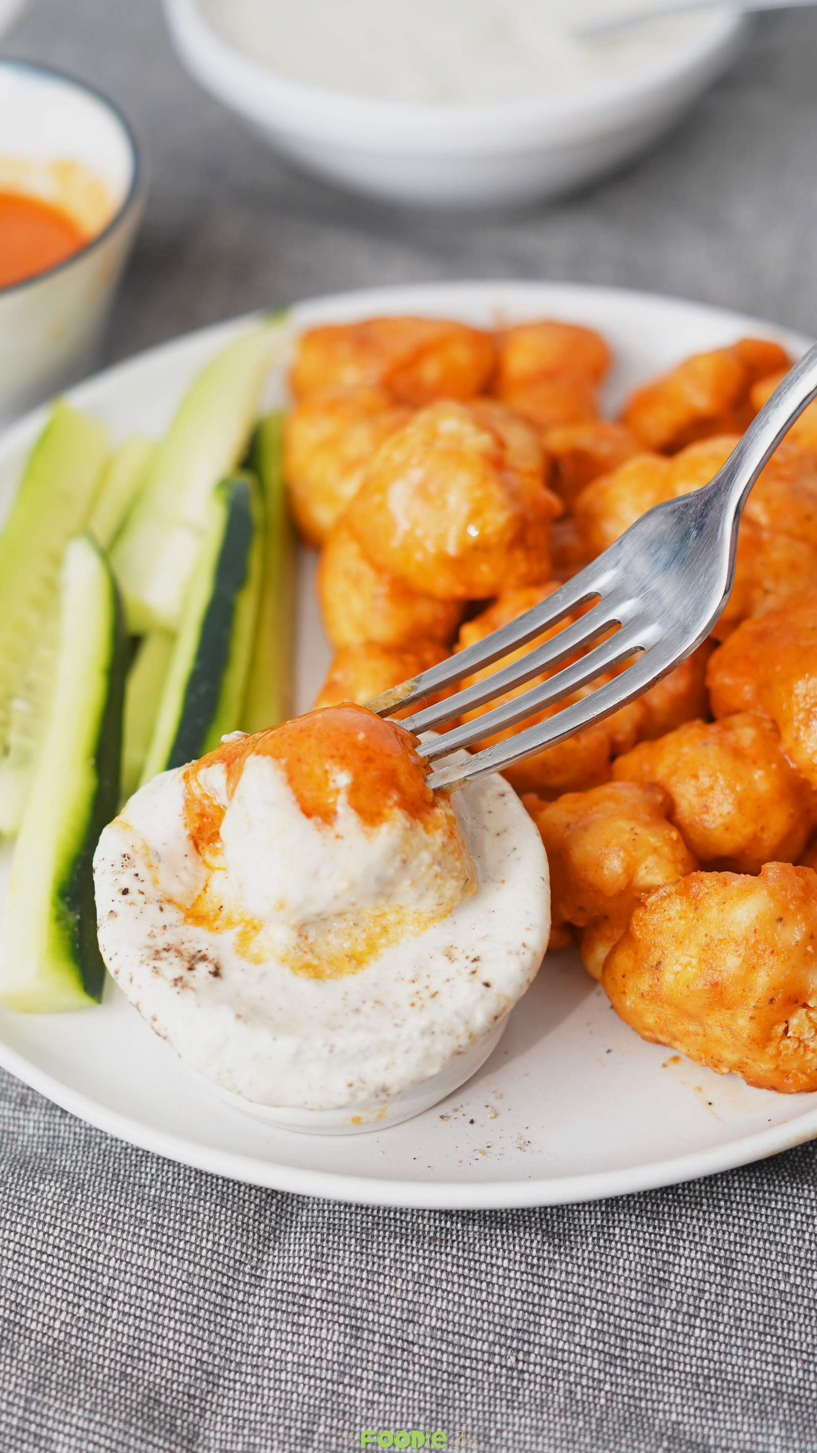 Buffalo cauliflower bites served with cucumber slices and creamy yogurt dip on a white plate.