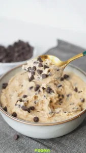 Golden spoon holding a scoop of cottage cheese cookie dough with chocolate chips over a bowl of cookie dough.