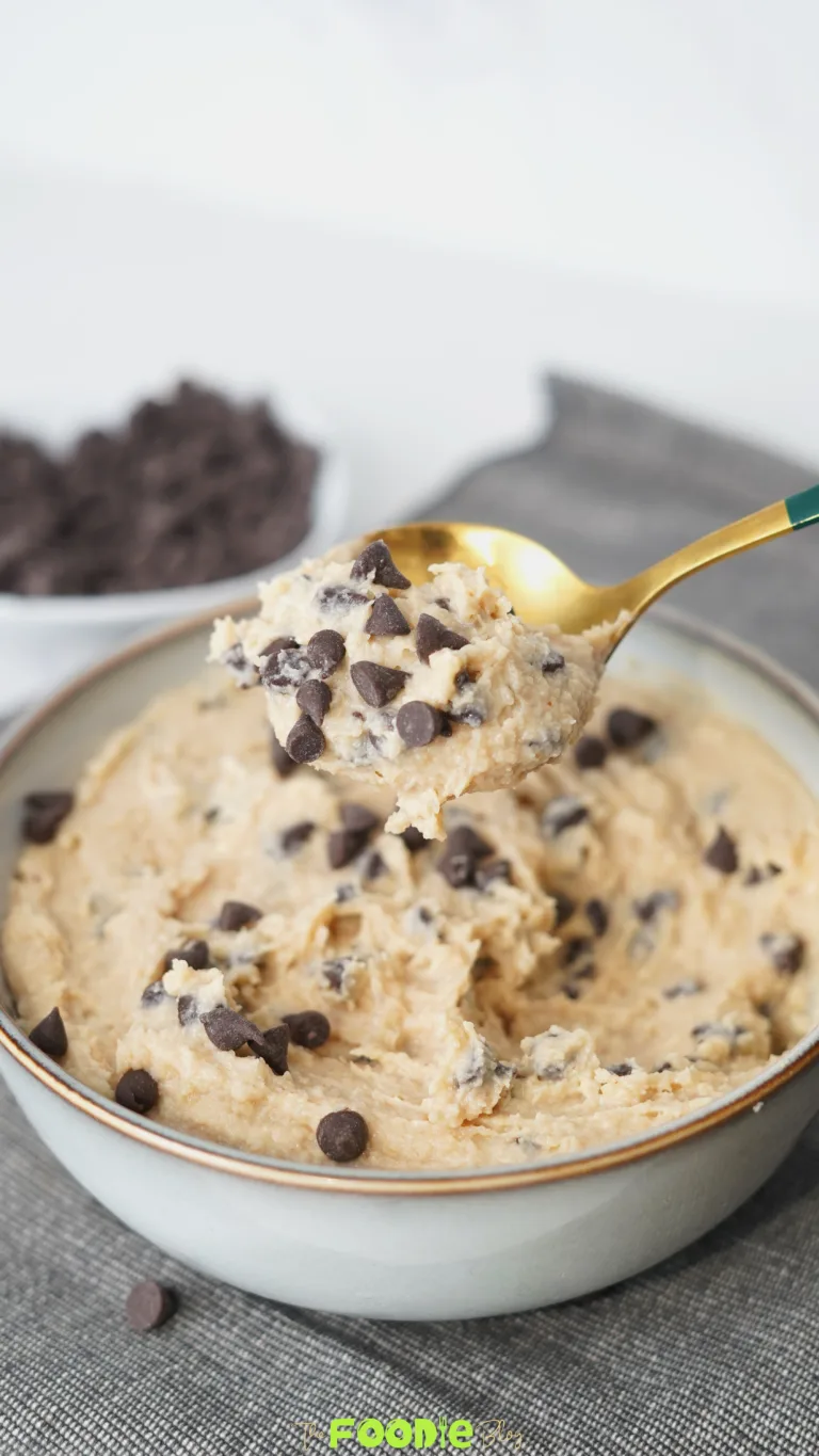Golden spoon holding a scoop of cottage cheese cookie dough with chocolate chips over a bowl of cookie dough.