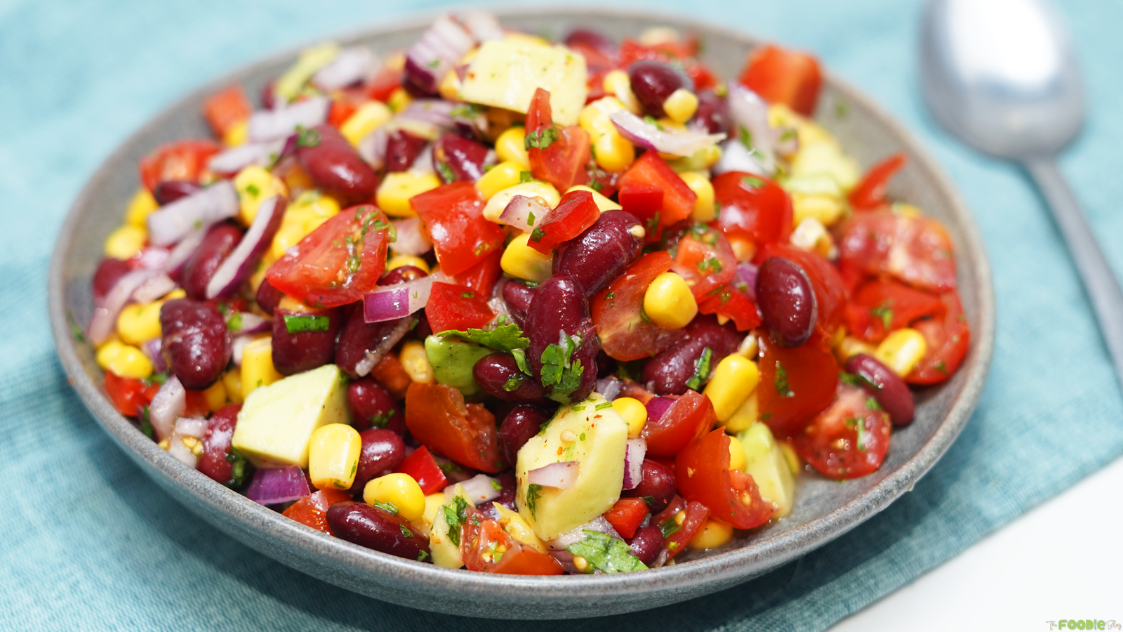 Cowboy bean salad served in a bowl with corn, beans, tomatoes, avocado, red onion, red bell pepper, and cilantro.