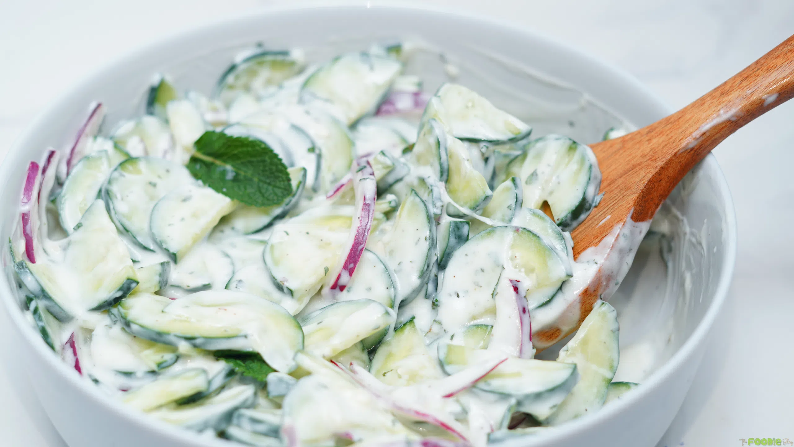 Close-up of sliced cucumbers and red onion coated in creamy lemon yogurt dressing with a wooden spoon.