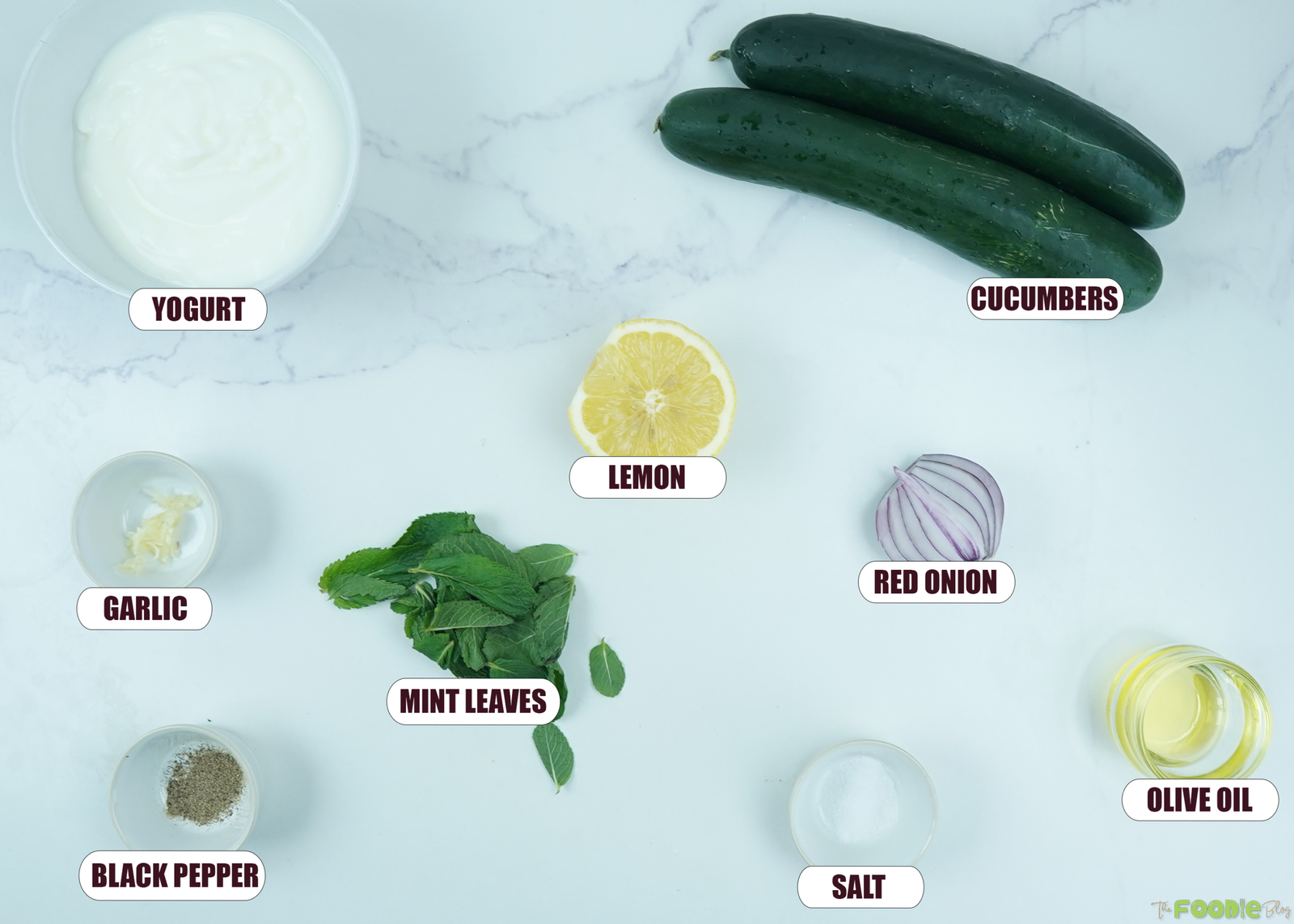 Ingredients for creamy cucumber salad including yogurt, cucumbers, lemon, red onion, mint, garlic, olive oil, salt, and black pepper.