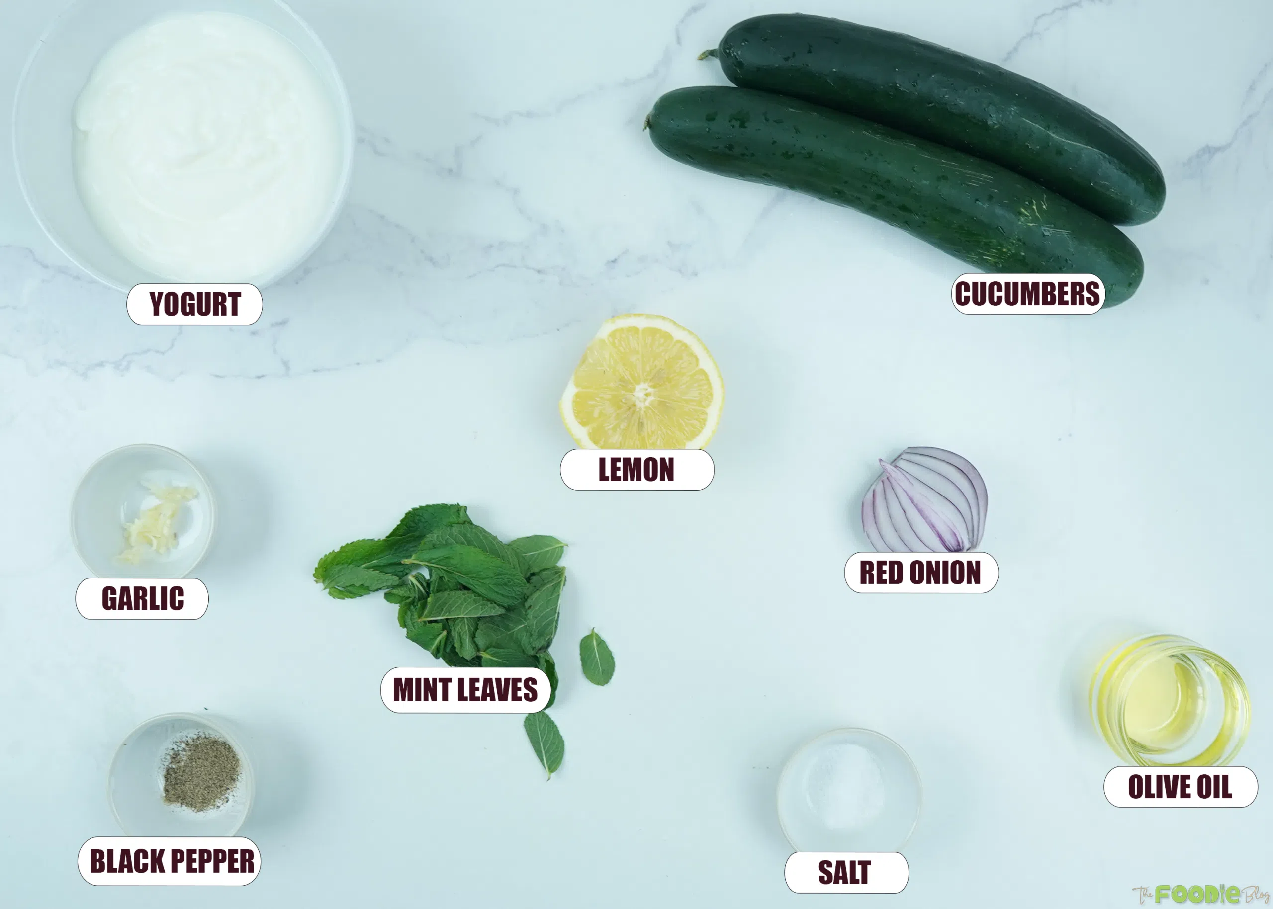 Ingredients for creamy cucumber salad including yogurt, cucumbers, lemon, red onion, mint, garlic, olive oil, salt, and black pepper.