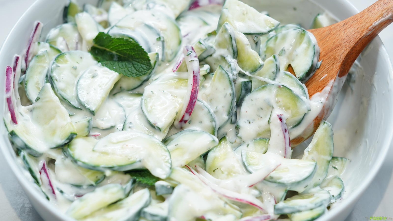 Creamy cucumber salad with red onion and mint tossed in lemon yogurt dressing in a white bowl.