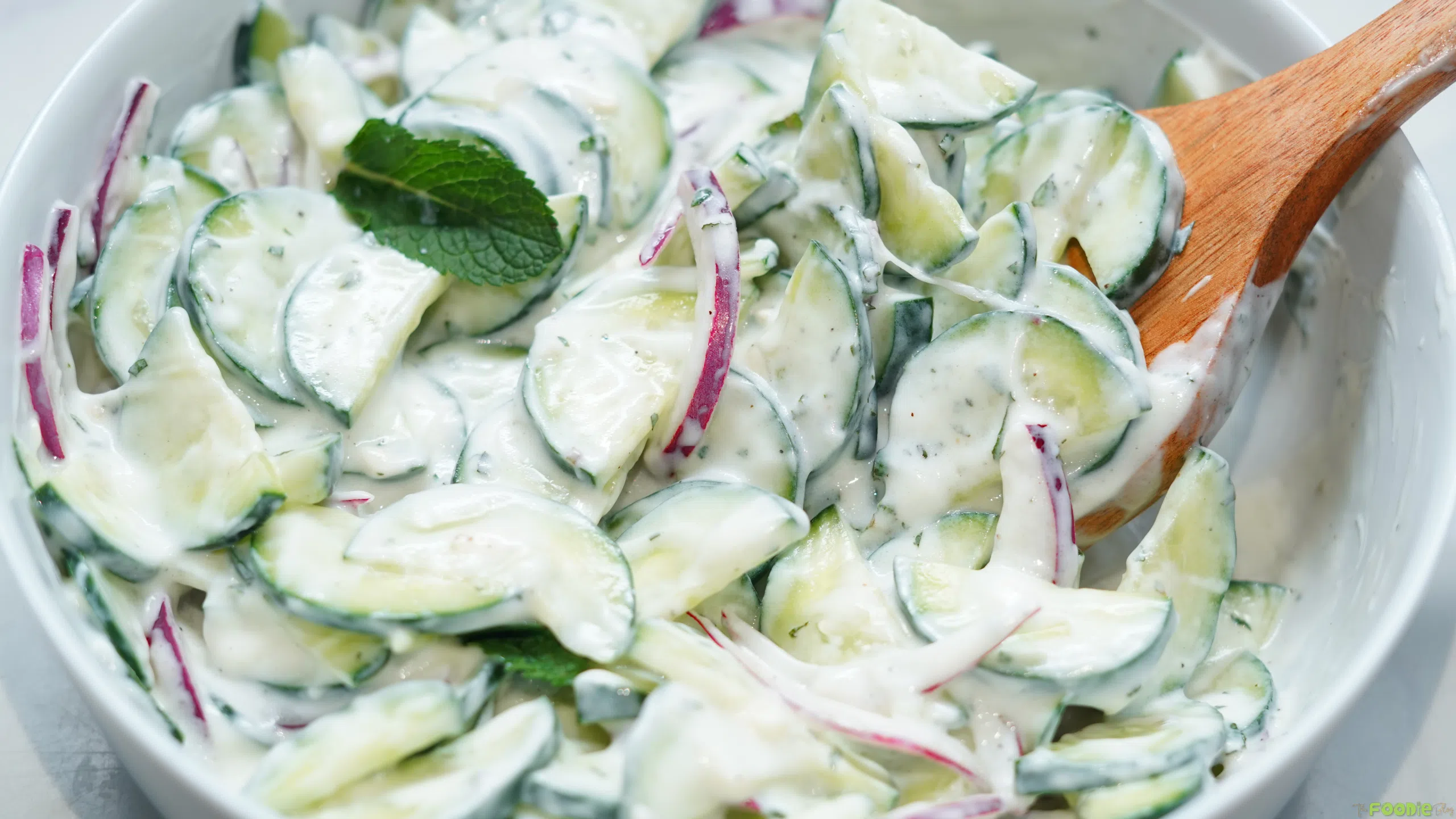 Creamy cucumber salad with red onion and mint tossed in lemon yogurt dressing in a white bowl.
