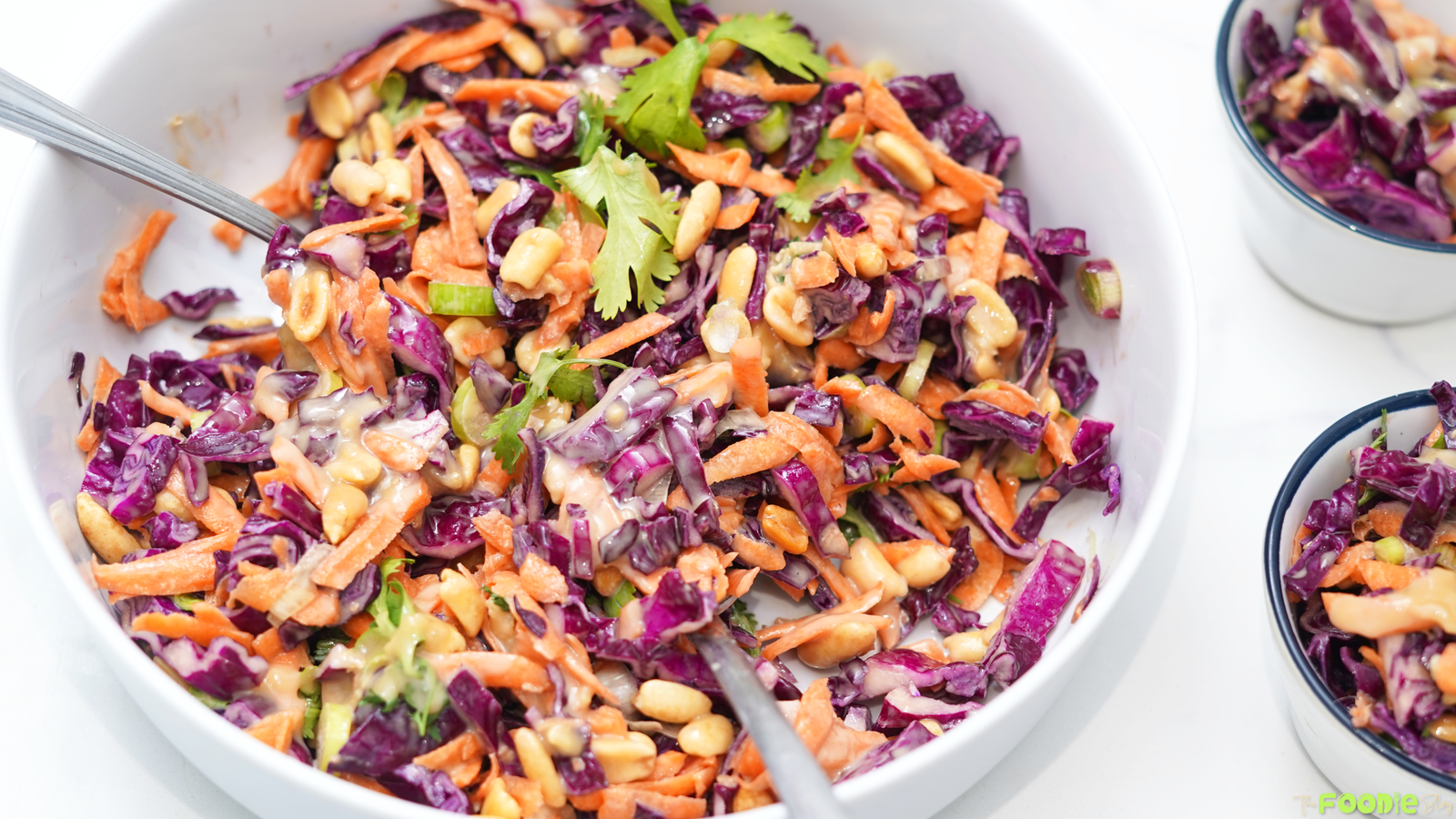 Overhead view of a purple cabbage and carrot salad topped with peanuts, cilantro leaves, green onions, and sesame ginger dressing.
