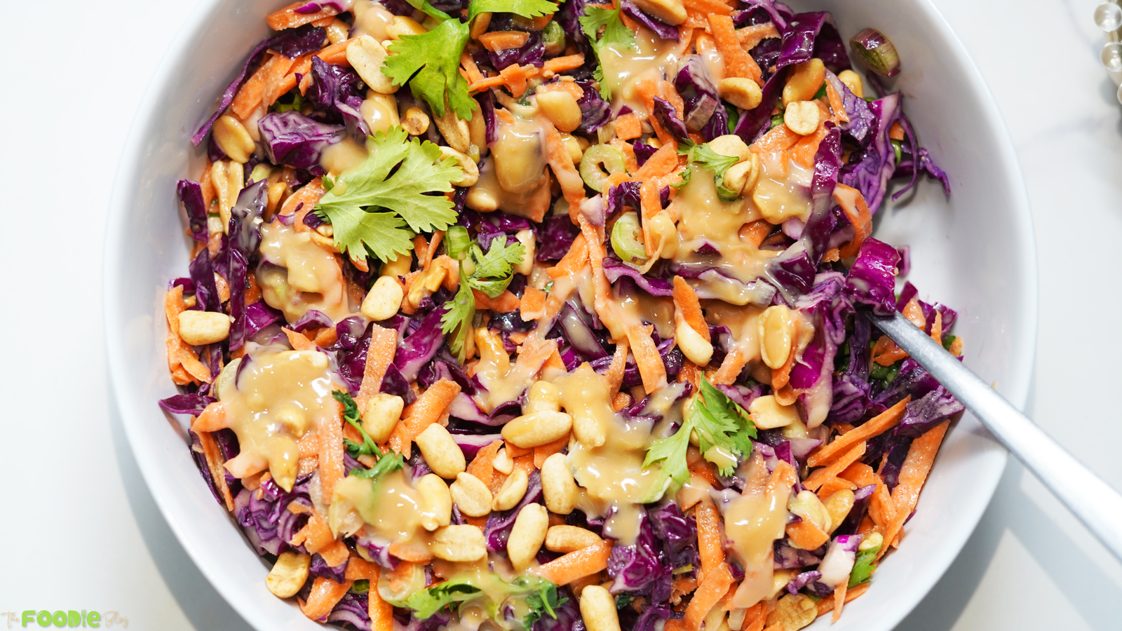 Colorful crunchy cabbage salad in a white bowl with shredded purple cabbage, carrots, peanuts, cilantro, and sesame ginger dressing.